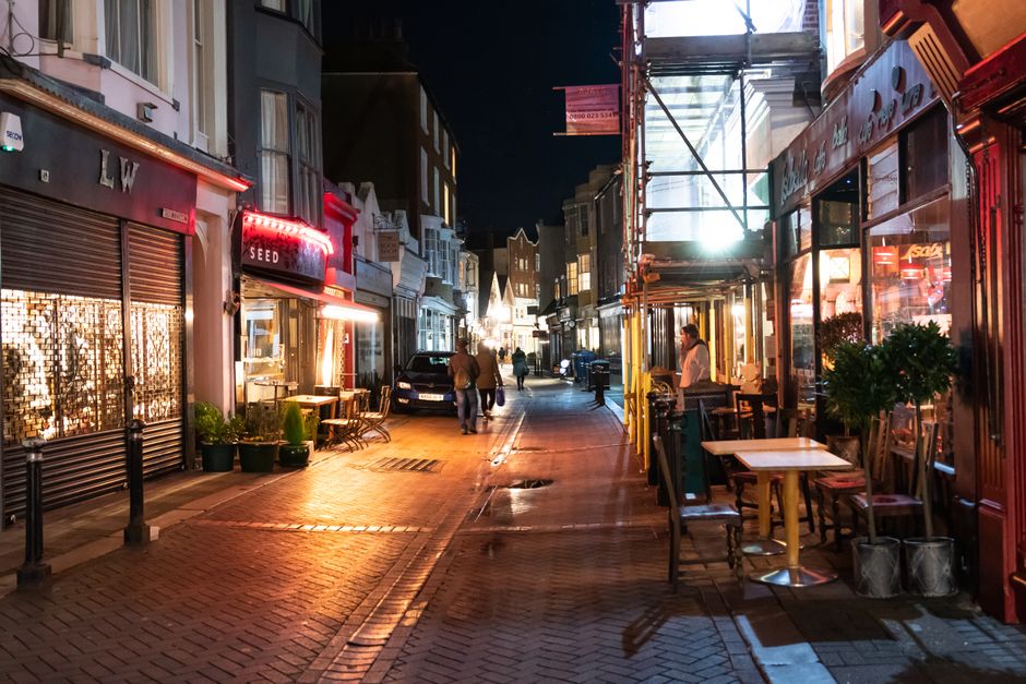 A street scene on Barnes High Street showing a row of traditional brick storefronts and residential buildings with large windows and white trims, some under construction with scaffolding and protectiv
