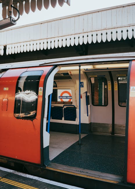 The image shows the open sliding door of a red London Underground train at a station platform. Inside the train, black fabric-covered seats are visible along with blue and grey grab handles. The platf